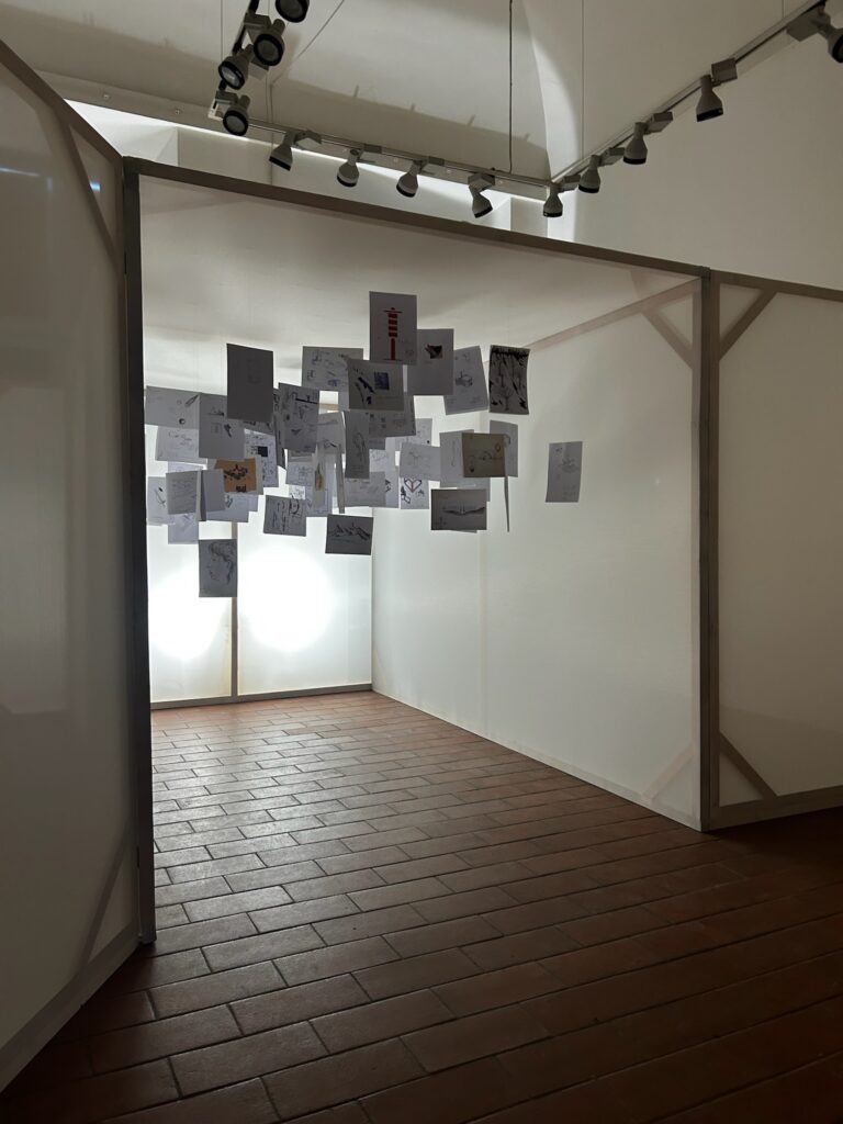 Foto dellinstallazione stanza dell'artista con i disegni appesi al soffitto